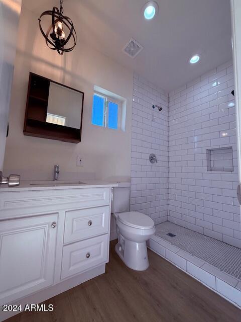 bathroom featuring a tile shower, hardwood / wood-style floors, vanity, and toilet