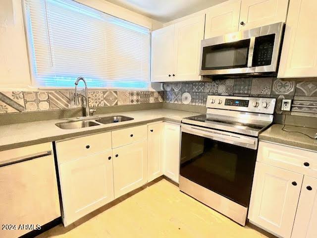 kitchen with stainless steel appliances, white cabinetry, tasteful backsplash, and sink