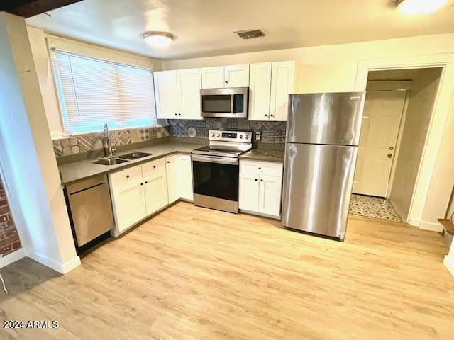 kitchen featuring white cabinetry, sink, light hardwood / wood-style flooring, backsplash, and appliances with stainless steel finishes