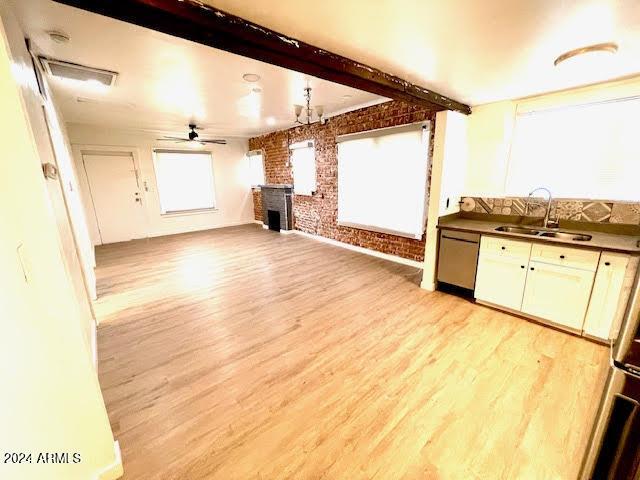 unfurnished living room featuring ceiling fan, light wood-type flooring, sink, and brick wall