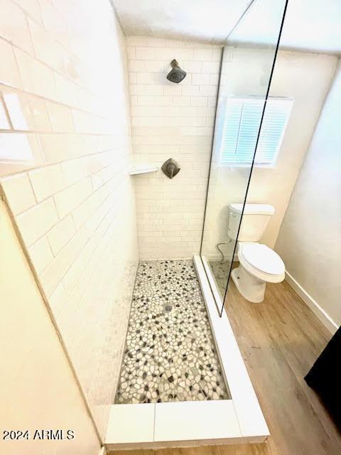 bathroom featuring a tile shower, hardwood / wood-style flooring, and toilet