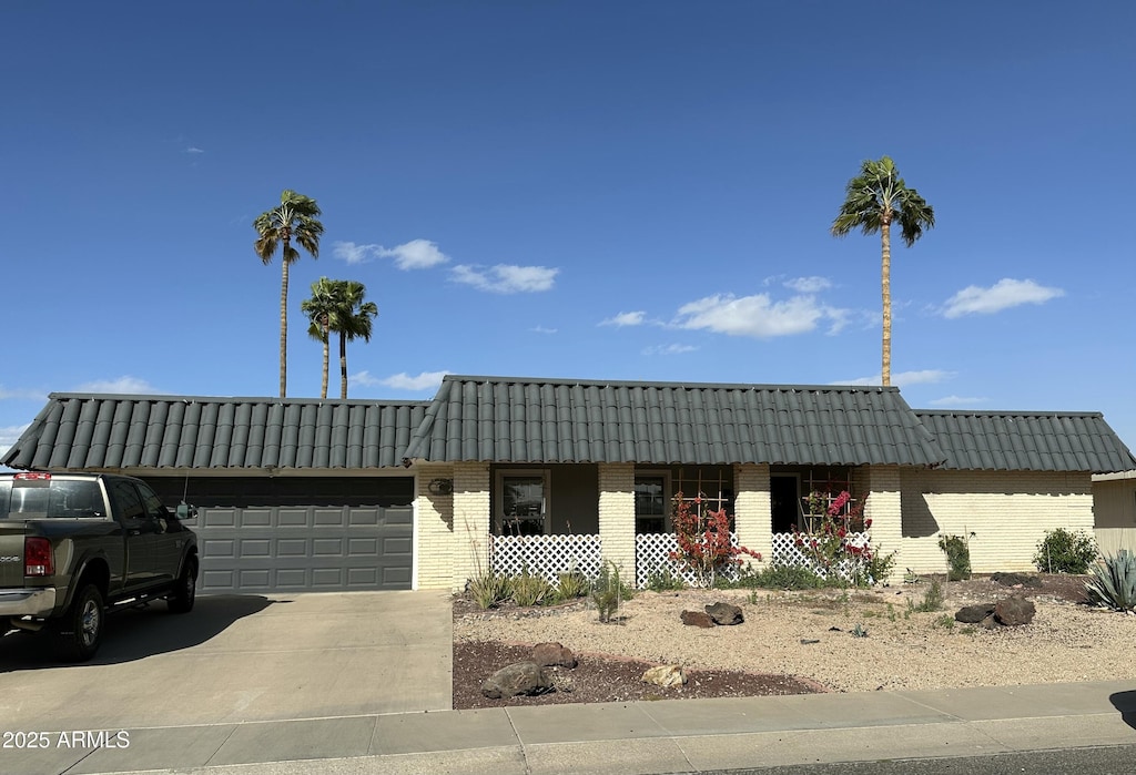 view of front facade featuring a tile roof, a porch, concrete driveway, a garage, and brick siding