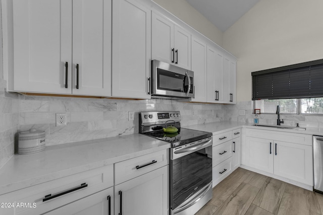 kitchen with appliances with stainless steel finishes, sink, white cabinets, decorative backsplash, and light hardwood / wood-style flooring