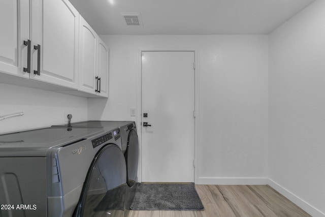 laundry area with cabinets, washing machine and clothes dryer, and light wood-type flooring