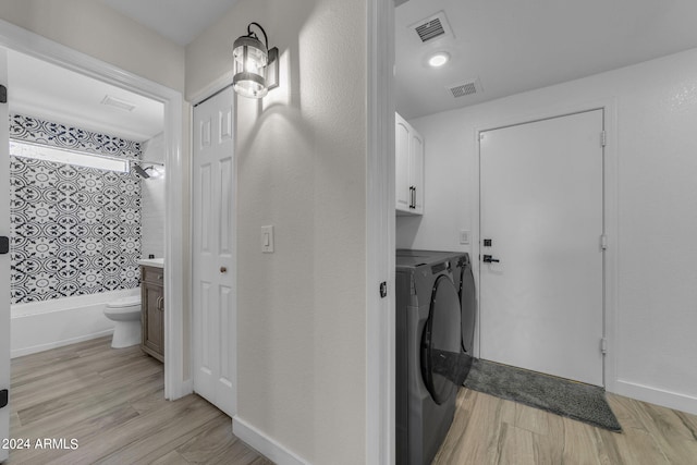 laundry room with cabinets, washing machine and clothes dryer, and light hardwood / wood-style flooring