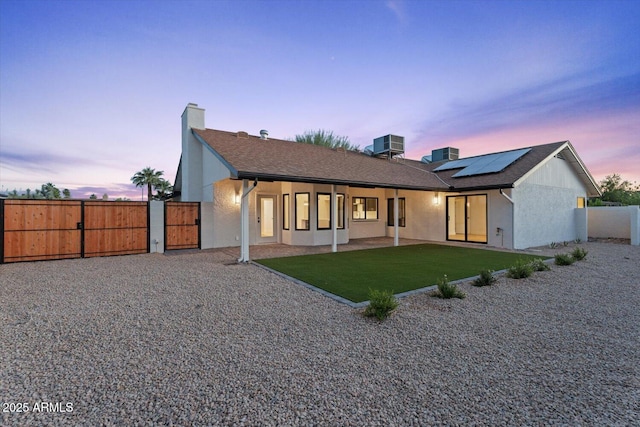 6228 E Blanche Dr, Scottsdale, AZ 85254 - back of house at dusk featuring a gate, a chimney, solar panels, and stucco siding