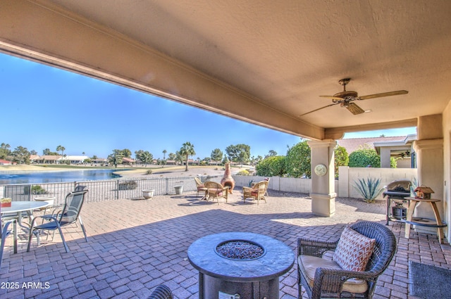 view of patio featuring a water view, ceiling fan, an outdoor fire pit, and a grill