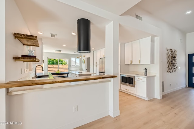 kitchen featuring kitchen peninsula, light hardwood / wood-style flooring, stainless steel appliances, extractor fan, and white cabinets