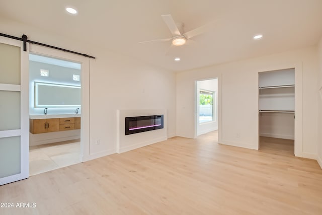 unfurnished living room featuring sink, light hardwood / wood-style floors, ceiling fan, and a barn door