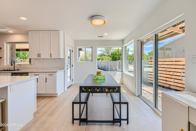 kitchen with a wealth of natural light, light hardwood / wood-style flooring, white cabinetry, and sink