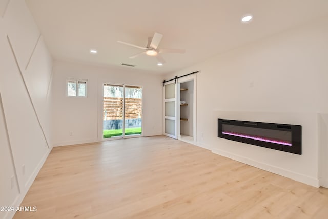 unfurnished living room featuring light hardwood / wood-style floors, ceiling fan, and a barn door