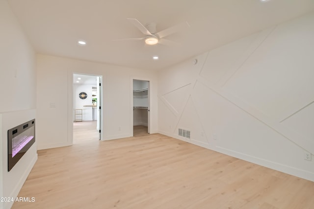 unfurnished bedroom featuring a spacious closet, a closet, light hardwood / wood-style flooring, and ceiling fan