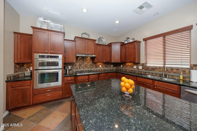 kitchen with stainless steel appliances, sink, backsplash, and dark stone counters