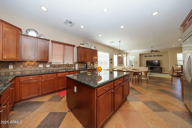 kitchen with sink, decorative light fixtures, a center island, dark stone counters, and decorative backsplash