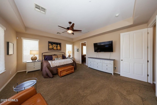 bedroom with a raised ceiling, multiple windows, and dark colored carpet