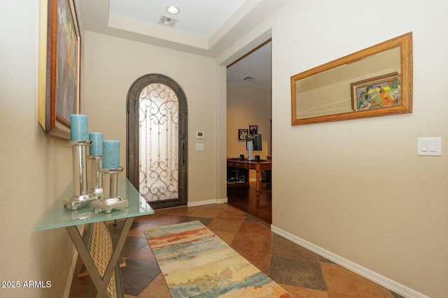 foyer featuring a raised ceiling and dark tile patterned floors