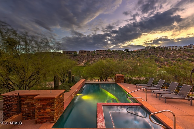 pool at dusk with a patio area and an in ground hot tub