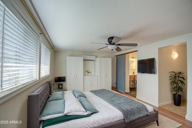 bedroom featuring a textured ceiling, light hardwood / wood-style floors, a wall unit AC, and ceiling fan