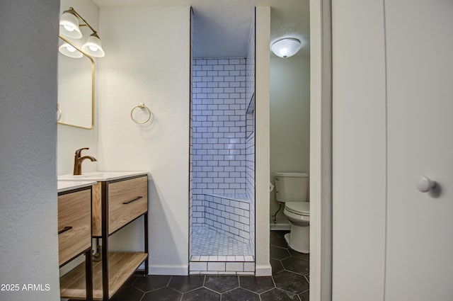 bathroom with toilet, a tile shower, vanity, and tile patterned floors