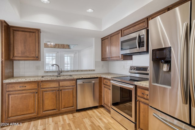 kitchen with stainless steel appliances, light stone counters, light hardwood / wood-style floors, and sink