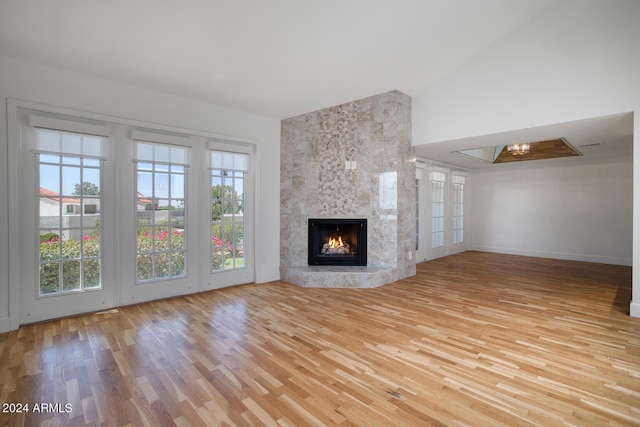 unfurnished living room featuring high vaulted ceiling, a fireplace, light hardwood / wood-style flooring, and plenty of natural light