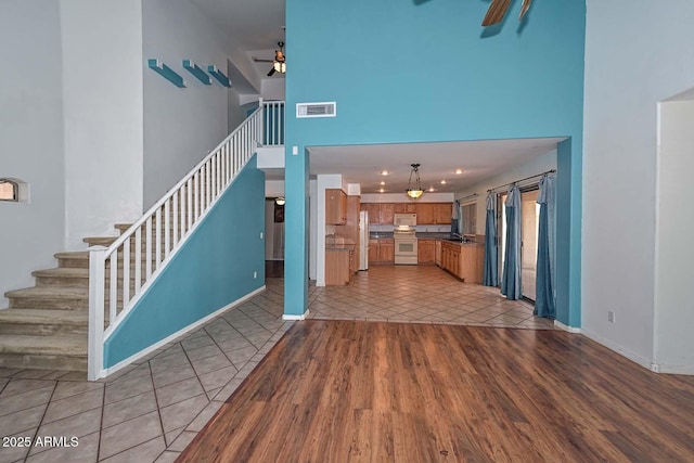 16828 W Windermere Way, Surprise, AZ 85374 - unfurnished living room featuring a ceiling fan, a towering ceiling, stairs, and light wood-style flooring