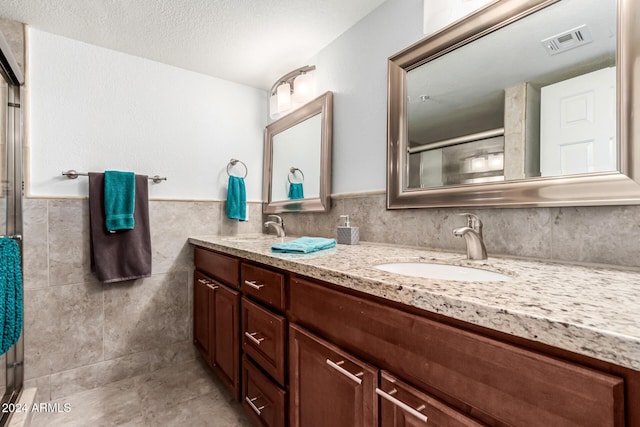 bathroom with an enclosed shower, vanity, tile walls, and a textured ceiling