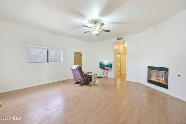 living area with ceiling fan, light wood-style flooring, baseboards, and a glass covered fireplace