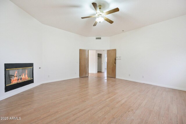 unfurnished living room featuring light wood-style floors, a ceiling fan, a glass covered fireplace, and baseboards