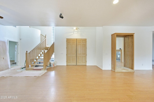 unfurnished living room featuring light wood-type flooring and stairway