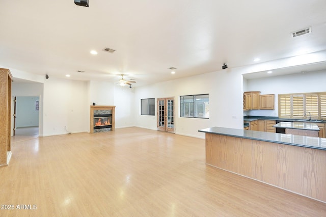 unfurnished living room featuring a ceiling fan, recessed lighting, a glass covered fireplace, light wood-style flooring, and baseboards