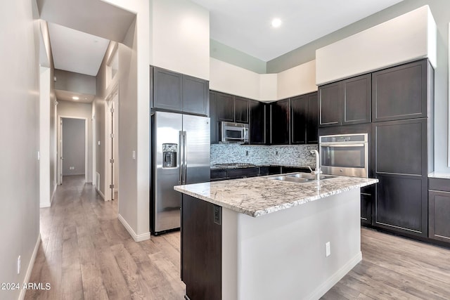 kitchen featuring light hardwood / wood-style floors, a kitchen island with sink, sink, decorative backsplash, and stainless steel appliances