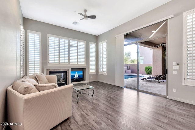 living area featuring wood-type flooring, ceiling fan, a fireplace, and a healthy amount of sunlight