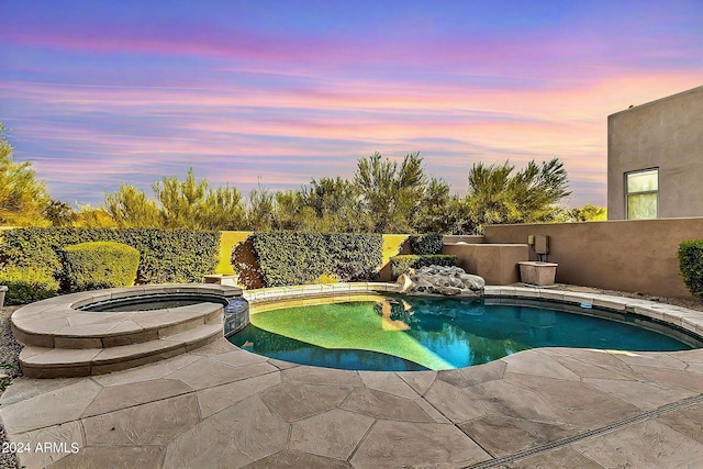 pool at dusk featuring an in ground hot tub and a patio area