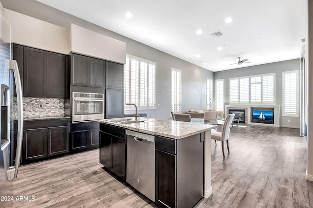 kitchen featuring decorative backsplash, stainless steel appliances, light wood-type flooring, ceiling fan, and sink