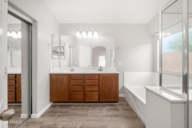 1015 E Penny Ln, San Tan Valley, AZ 85140 - bathroom featuring double vanity, a garden tub, wood finished floors, and baseboards