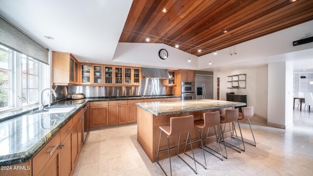 kitchen with a center island, dark stone counters, wall chimney range hood, appliances with stainless steel finishes, and wood ceiling