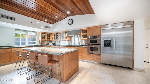 kitchen with light stone countertops, wall chimney exhaust hood, wooden ceiling, stainless steel appliances, and a kitchen island