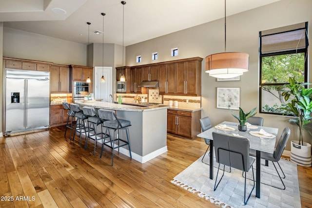 kitchen featuring a kitchen island with sink, a breakfast bar area, hanging light fixtures, built in appliances, and tasteful backsplash