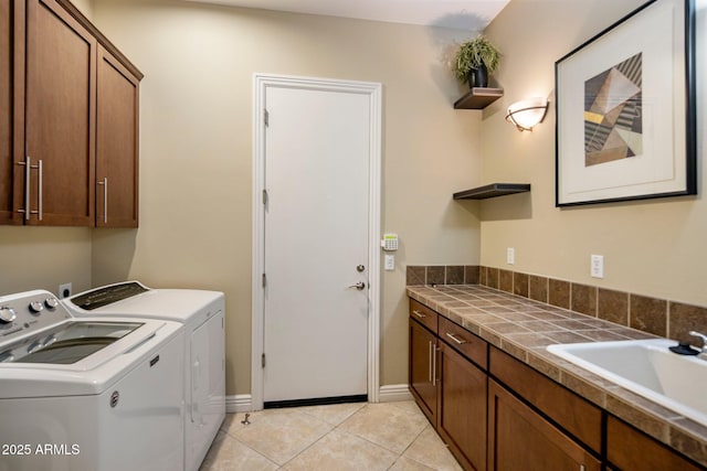 laundry area featuring sink, washing machine and dryer, light tile patterned floors, and cabinets