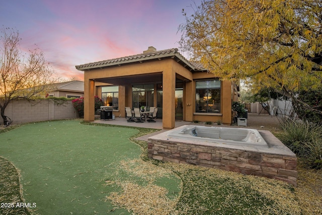 back house at dusk featuring a patio area, a lawn, and a hot tub