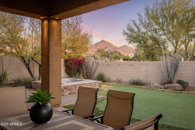 patio terrace at dusk featuring a jacuzzi, a yard, and a mountain view