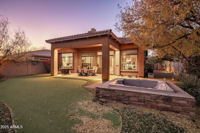 back house at dusk with a patio area and an outdoor hot tub