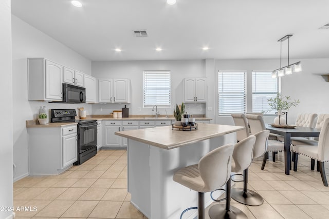 kitchen featuring decorative light fixtures, black appliances, white cabinets, and plenty of natural light