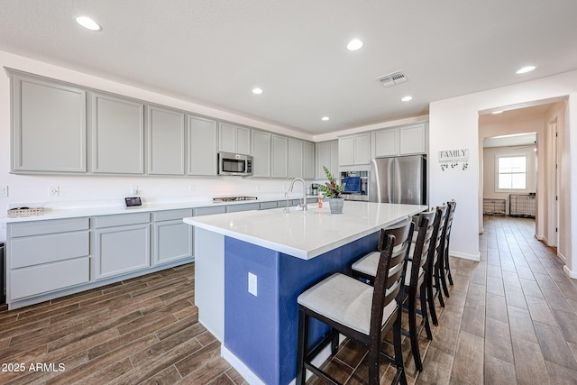 25051 N 140th Dr, Surprise, AZ 85387 - kitchen featuring stainless steel appliances, wood finish floors, gray cabinets, a kitchen bar, and recessed lighting