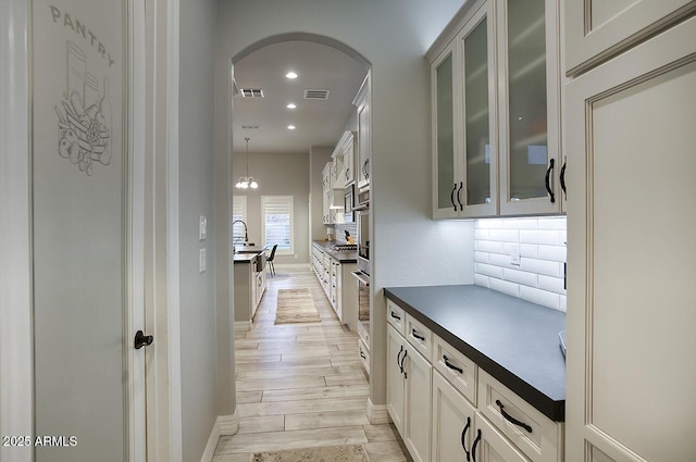 kitchen with glass insert cabinets, dark countertops, visible vents, and hanging light fixtures