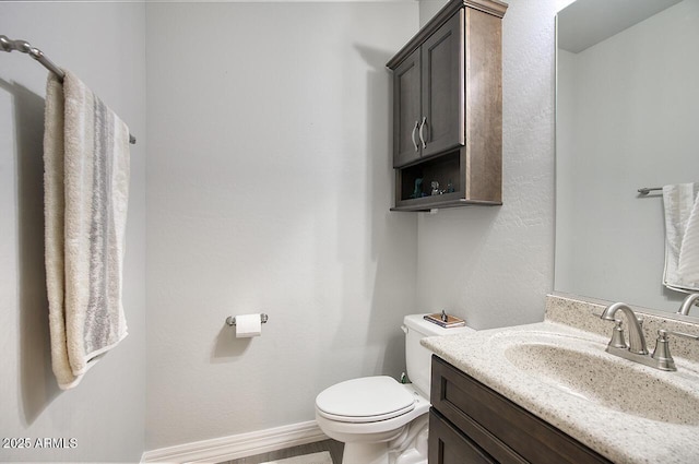 half bath featuring toilet, vanity, and baseboards