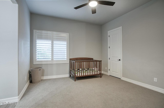 bedroom featuring a nursery area, light colored carpet, ceiling fan, and baseboards