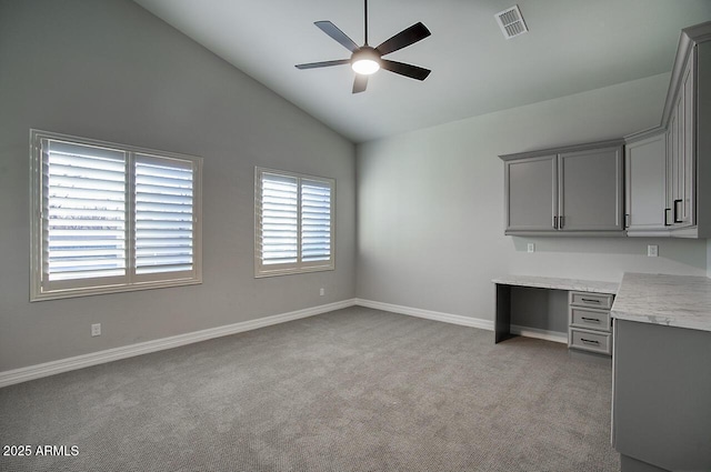 unfurnished office with lofted ceiling, light carpet, visible vents, a ceiling fan, and built in desk