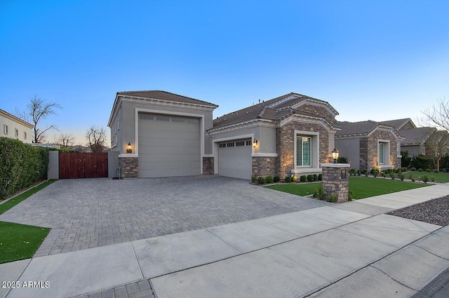 prairie-style house featuring an attached garage, fence, stone siding, decorative driveway, and stucco siding